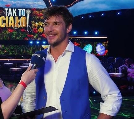 Mikołaj Roznerski z kawą, w swobodnej scenerii