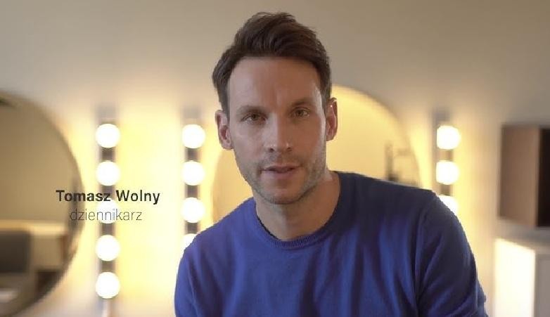 Tomasz Wolny w trakcie nagrania programu telewizyjnego, gestykulujący i nawiązujący kontakt z widzem.