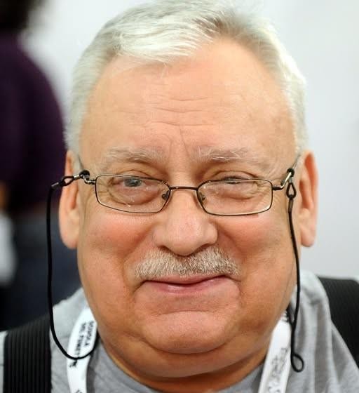 Zbiór symboli związanych z twórczością Andrzeja Sapkowskiego: otwarta księga z runami, wiedźmiński medalion, mapa fantasy i pióro.