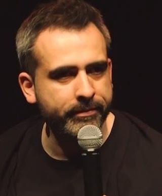 Abelard Giza podczas występu stand-upowego, z mikrofonem w dłoni.