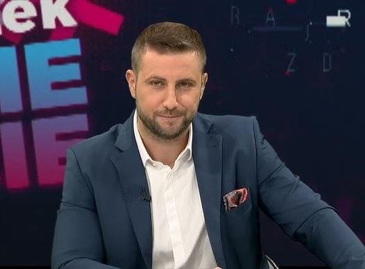 Miłosz Kłeczek prowadzący gorącą debatę polityczną w studiu telewizyjnym.